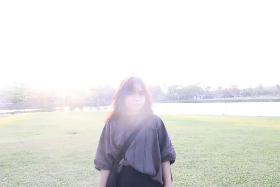 Daniele standing on a grassy field by the water, backlit by the late-afternoon sun
