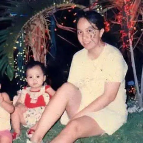 Old photo of a woman sitting on the grass with a baby, beneath decorative lights